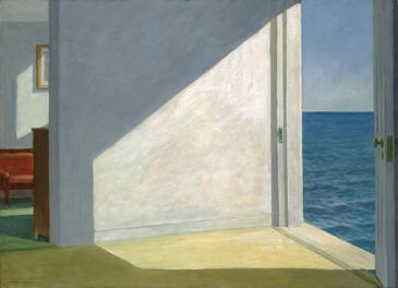 Sunlight falls into an empty room with a door opening directly onto the sea.