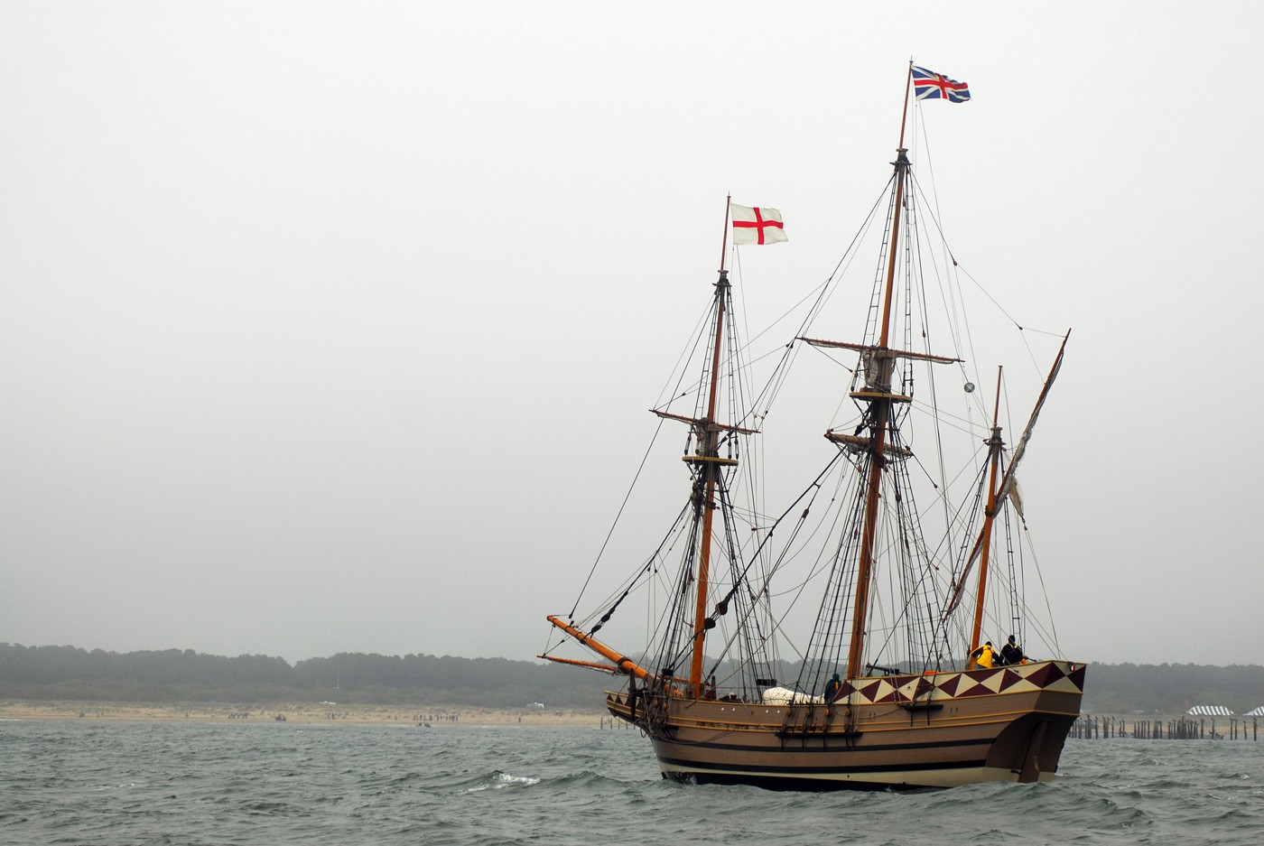 Modern Godspeed replica with tall masts, furled sails, rigging, and English flags on open water.