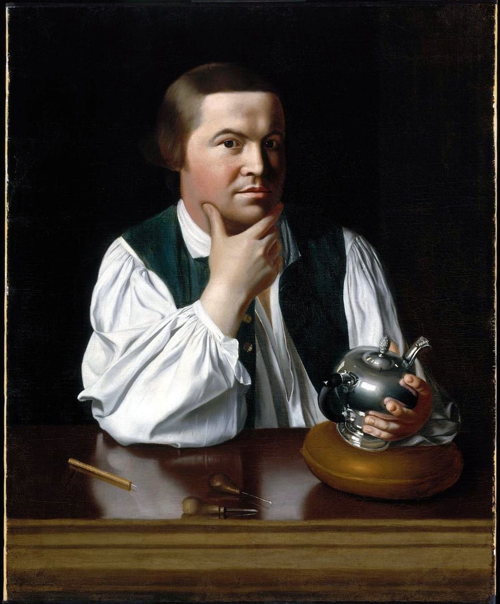Paul Revere, seated at a worktable, holds a silver teapot and rests his chin on one hand.